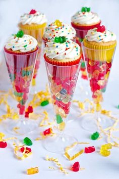 cupcakes with white frosting and sprinkles on them are sitting in wine glasses