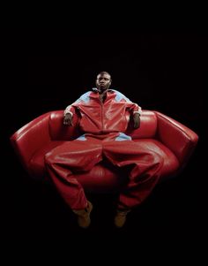 a man sitting on top of a red chair in the middle of a dark room