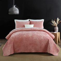 a bed with pink comforter and pillows in a room next to a black wall