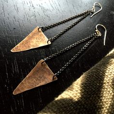 two triangle shaped earrings are hanging from chains on a black table with a striped blanket