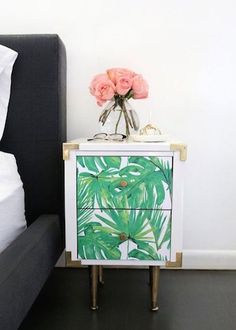 a nightstand with pink roses on it next to a black couch and white bedding