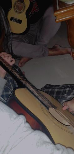 two people sitting on the floor playing guitar together, one person is holding an acoustic guitar