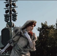 a woman dressed in period clothing standing next to a street light with her hands on her hips