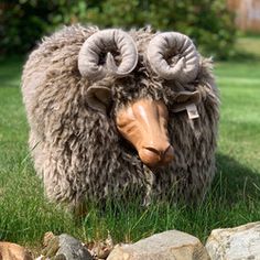 a sheep with horns standing in the grass near some rocks and trees, looking at the camera