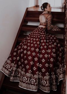 a woman in a maroon and gold lehenga sitting on some stairs with her back turned to the camera