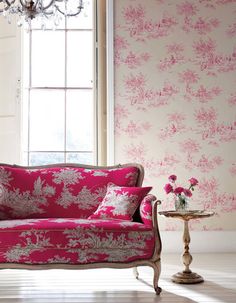 a pink couch sitting in front of a window next to a table with flowers on it