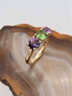 CJ122787AGRT Three stone Maine gemstone ring. Vibrant tourmaline and amethyst are set in this timeless 10k yellow gold three stone ring mounting. Green tourmaline is .60ct, Amethyst total weight is 1.3cts. Currently the ring is size 6.5 but we can resize at no extra charge, please specify ring size at checkout if needed. Green Multi-stone Amethyst Ring, Yellow Gold Multi-stone Amethyst Ring, Amethyst Three Stone Round Ring, 14k Gold Multi-stone Amethyst Ring, Amethyst Three Stone Ring, Green Amethyst Ring With Prong Setting, Three Stone Amethyst Ring, Amethyst And Diamond Ring, Ring Mountings