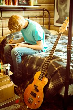 a person sitting on a bed writing in a notebook with an electric guitar next to them