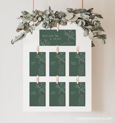 the seating chart is hanging on a white frame with eucalyptus leaves and wooden pegs