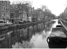 black and white photograph of a boat on the water in front of buildings with cars parked along side it