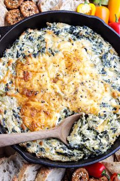 spinach dip in a cast iron skillet surrounded by bread, tomatoes and crackers