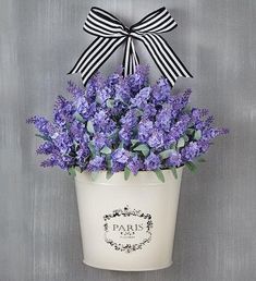 purple flowers in a white pot with a black bow on the top and paris logo