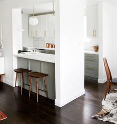 an open kitchen and dining room with white walls, wood flooring and wooden stools