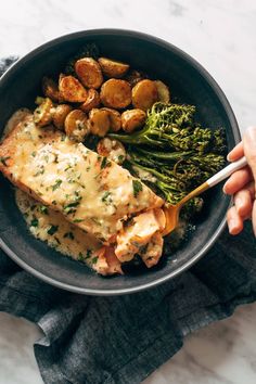 someone is holding a fork in a bowl with chicken, broccoli and potatoes