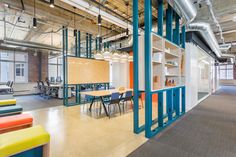 an open office space with tables, chairs and shelves on the wall in front of windows