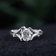 a close up view of a ring with an oval cut diamond in the center and leaves around it