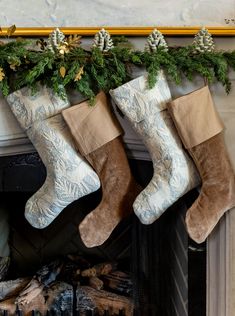 three stockings hanging from a mantel with pine cones on top and evergreen branches above