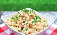 a white bowl filled with macaroni salad on top of a checkered table cloth