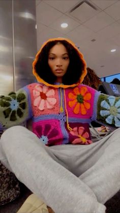 a woman sitting on the floor with her legs crossed wearing a colorful sweater and pants