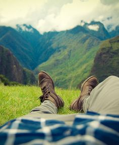 a man laying on top of a lush green field next to mountains with a quote above it