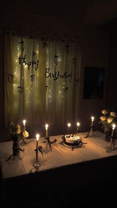 a birthday cake with lit candles sitting on a table in front of a curtained window