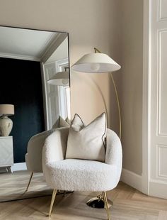 a white chair sitting next to a mirror in a living room under a light fixture