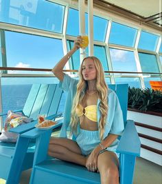 a woman sitting in a blue chair drinking from a glass on the deck of a cruise ship