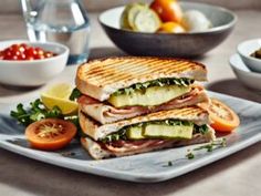 a sandwich cut in half sitting on top of a plate next to bowls of fruit