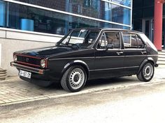 an old black car parked on the side of the road in front of a building