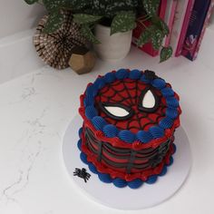 a spiderman cake sitting on top of a white plate next to a potted plant