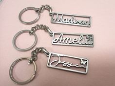 three personalized metal key chains with name tags attached to them on a pink background