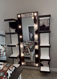 a mirror with lights on it in a bedroom next to a night stand and bed