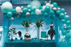 a table topped with balloons and cake next to a blue curtain filled with green, white and silver decorations