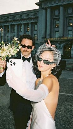 a man in a tuxedo holding a bouquet of flowers next to a woman wearing a veil