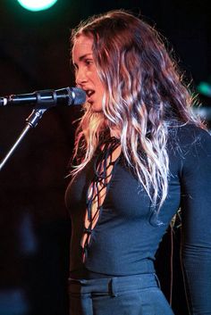 a woman with long hair standing in front of a microphone and singing into a mic