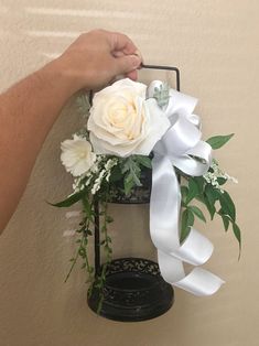 a person holding a white rose and greenery in front of a wall hanging decoration