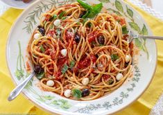 a plate of spaghetti with tomatoes, olives and basil