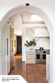 an archway leading into a kitchen with white walls and tile flooring, along with stainless steel appliances