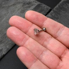 a tiny silver seashell shaped nose ring on someone's palm - like hand