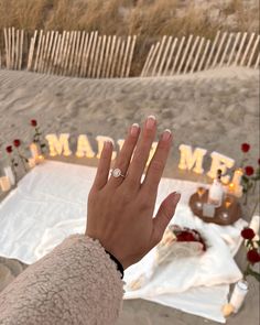 a woman's hand with a diamond ring on top of her finger at the beach