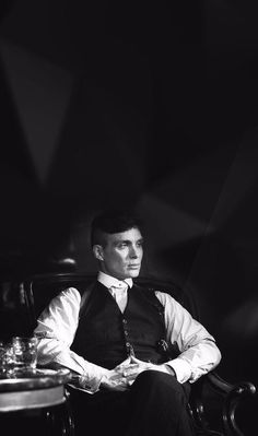 black and white photograph of a man sitting in a chair with his hands folded out