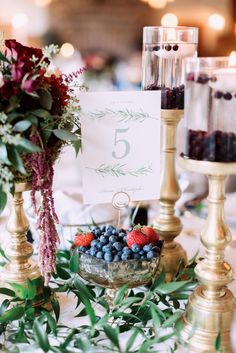 berries and blueberries are in a bowl on a table with gold candlesticks