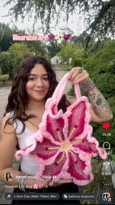 a woman holding up a pink crocheted flower