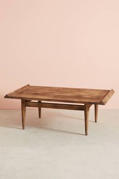 a wooden coffee table sitting on top of a white floor next to a pink wall