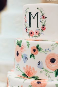 a three tiered cake decorated with flowers and the letter m on it's side