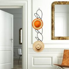 an orange hat hanging on the wall next to a chair and mirror in a white room