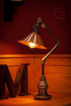 a desk lamp sitting on top of a wooden table next to the letter m in front of it