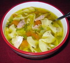 a red bowl filled with chicken noodle soup on top of a red place mat