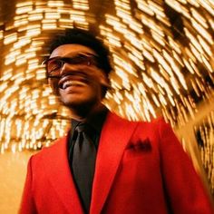 a man in a red jacket and black tie standing next to a wall with lights