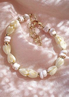 Flanked with natural white puka shells and pikake flowers, this unique shell bracelet evokes visions of Hawaii's white sands and soothing shores. Stack this gold bracelet with other beaded beauties and you'll be ready for your tropical escape.✦ DETAILS ✦✧ Name: Me'e (MAY aye) - Heroine.✧ Adjustable from 6.5"-8".✧ 6-7mm White Puka Shells.✧ Carved Resin Pikake Flowers.✧ 14kt Gold Filled with lobster clasp.✧ All Ke Aloha Jewelry pieces come packaged thoughtfully, beautifully, and ready for gift giv Handmade White Pearl Bracelet For Vacation, White Bohemian Beaded Shell Bracelets, White Adjustable Shell Necklace Spiritual Style, White Adjustable Shell Necklace For Spiritual Wear, White Adjustable Spiritual Shell Necklace, White Hand-strung Bracelets For Vacation, White Hand-strung Bracelet For Vacation, Hand-strung White Bracelets For Vacation, White Shell Pearl Bracelet For The Beach